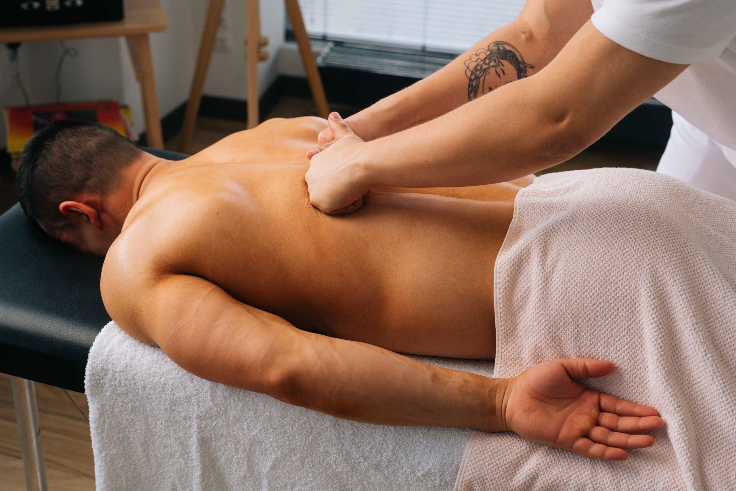 professional male masseur with strong tattooed hands massaging back with fist muscular sports man lying stomach massage table scaled